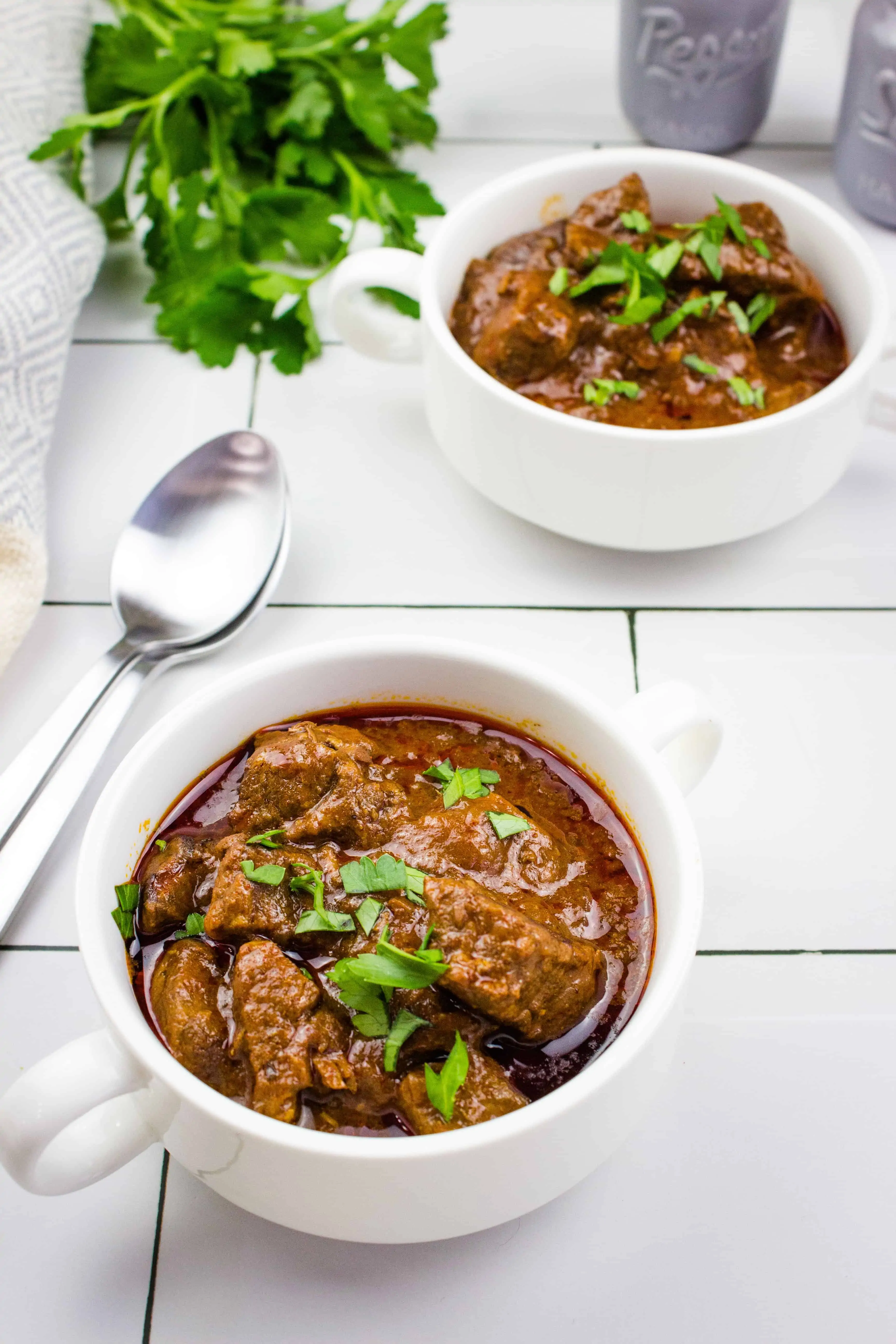 hungarian keto goulash in white serving bowls with parsley and spoons nearby