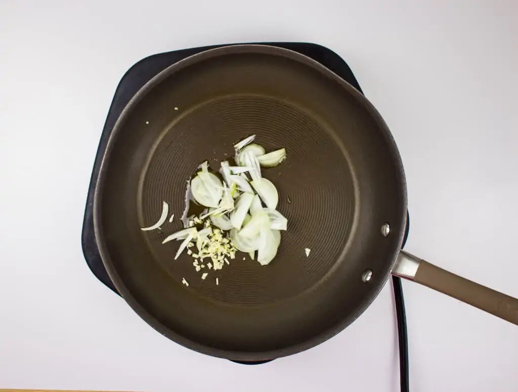 sauteeing the onions and garlic in a black skillet.
