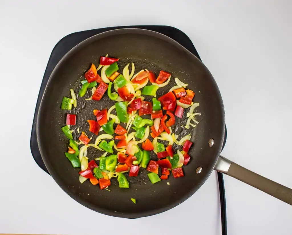 adding the red and green peppers to the sauteed onion to make ground turkey and peppers.