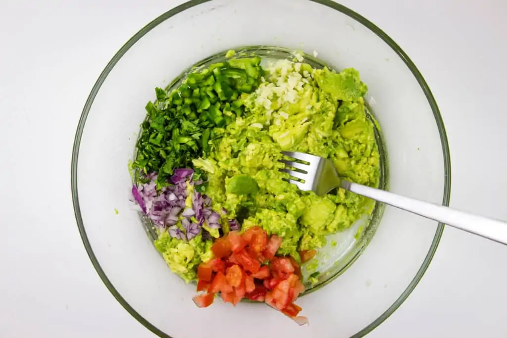 all ingredients in a bowl with a fork for mashing the avocado and stirring the ingredients