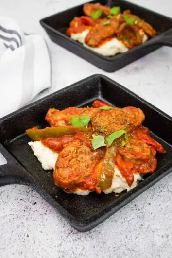 keto sausage stew in individual size black square dishes on a bed of mashed cauliflower