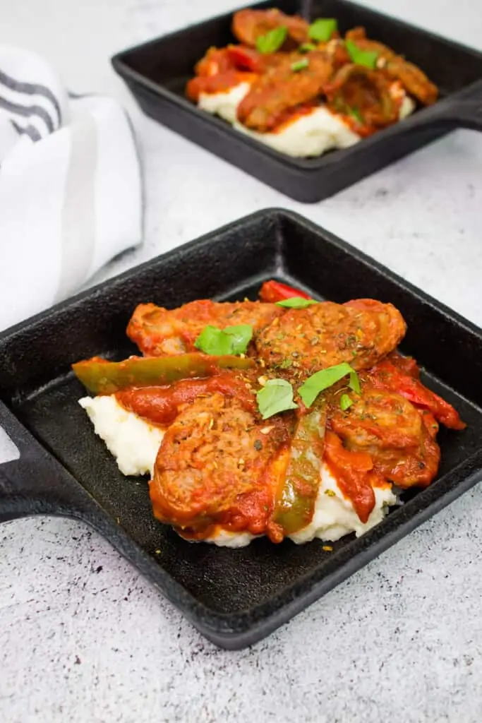 keto sausage stew in individual size black square dishes on a bed of mashed cauliflower