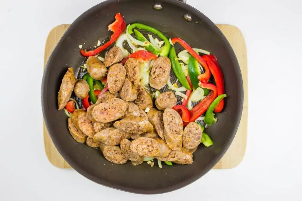 adding the sausage to the vegetables in the skillet