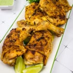 Oven-roasted Peruvian chicken on a platter with Peruvian chicken sauce in the background.