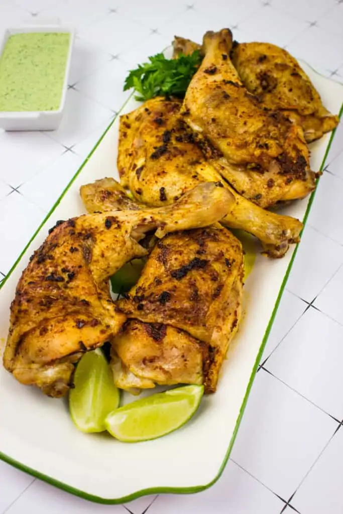 Oven-roasted Peruvian chicken on a platter with Peruvian chicken sauce in the background.