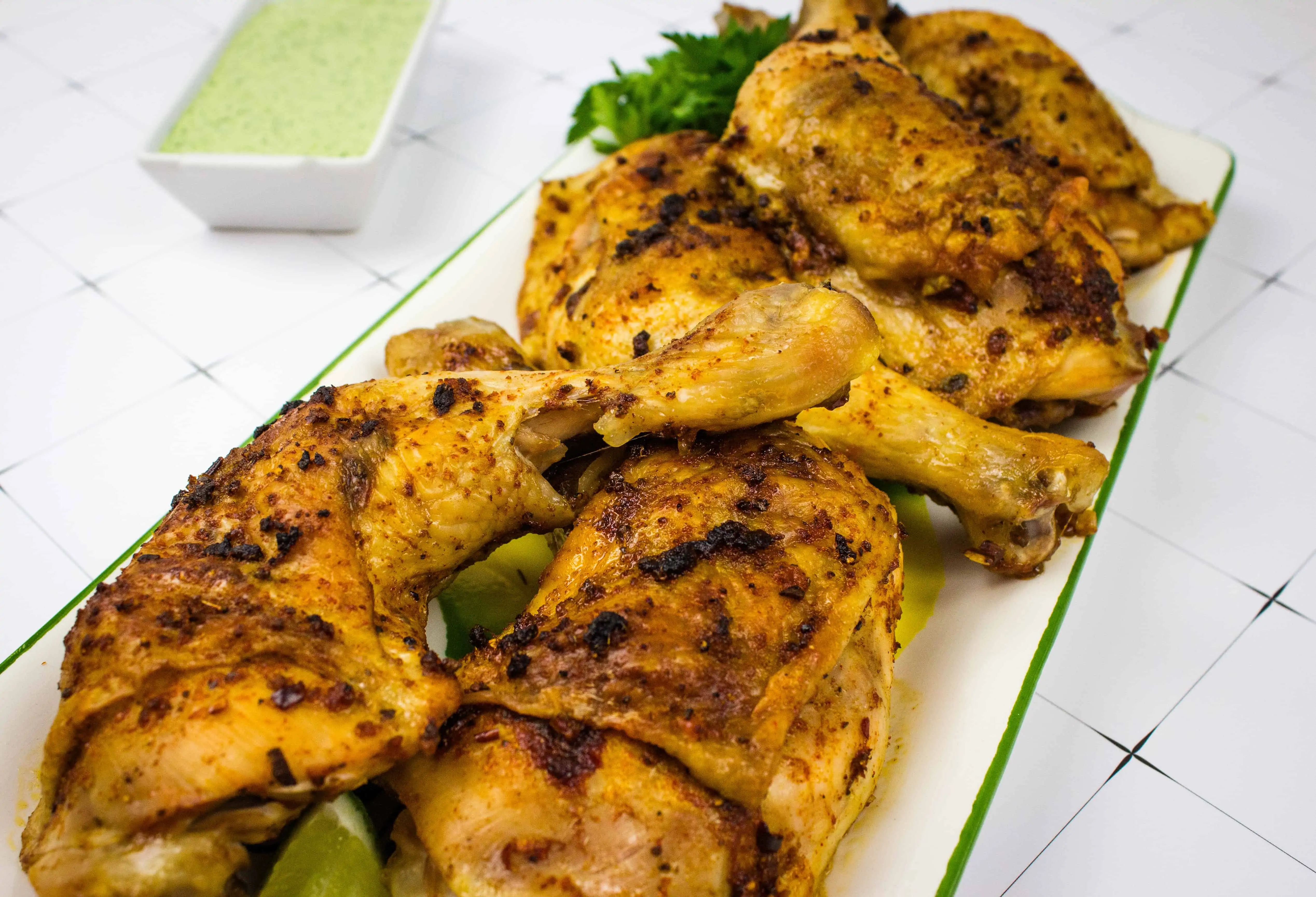 oven roasted peruvian chicken on a platter with green sauce in the background