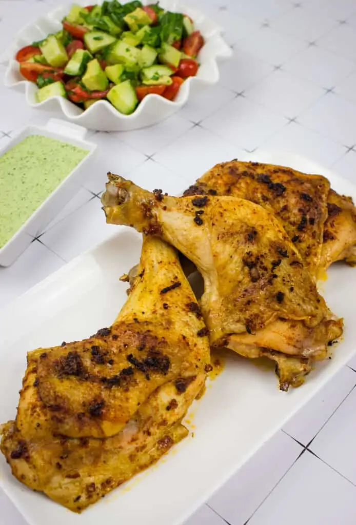oven roasted peruvian chicken with a tomato, cucumber and avocado salad in the background