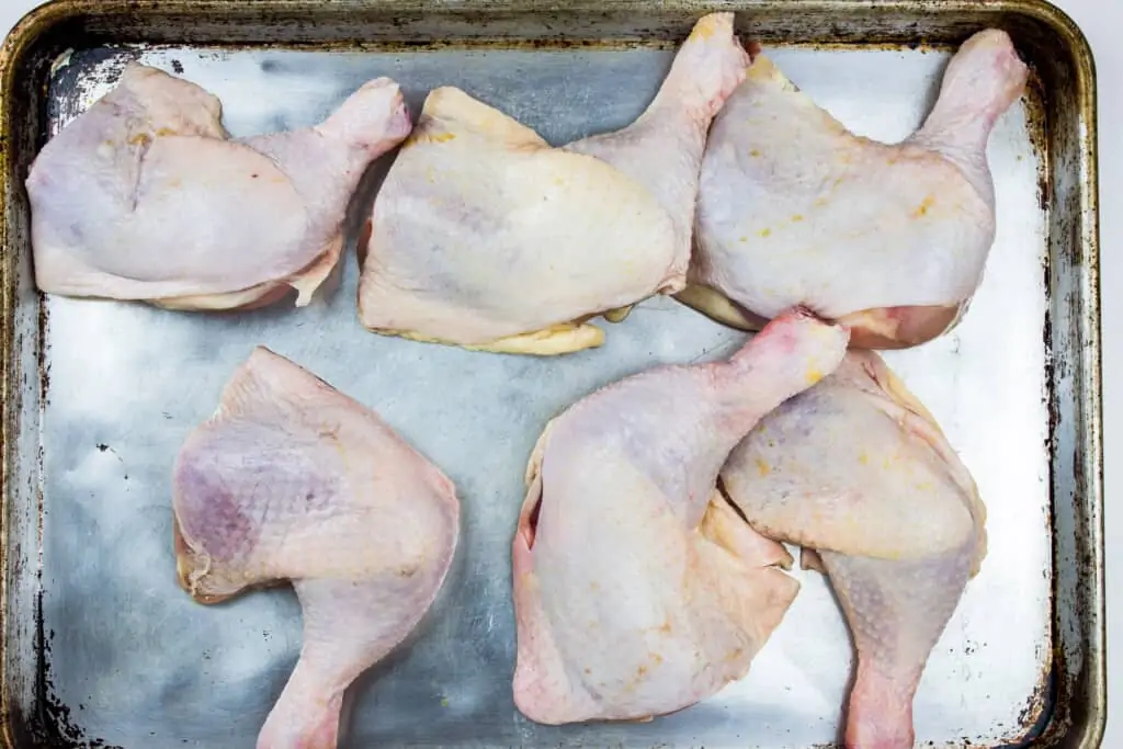 chicken leg quarters on a sheet pan ready to be rubbed with the spice mixture.