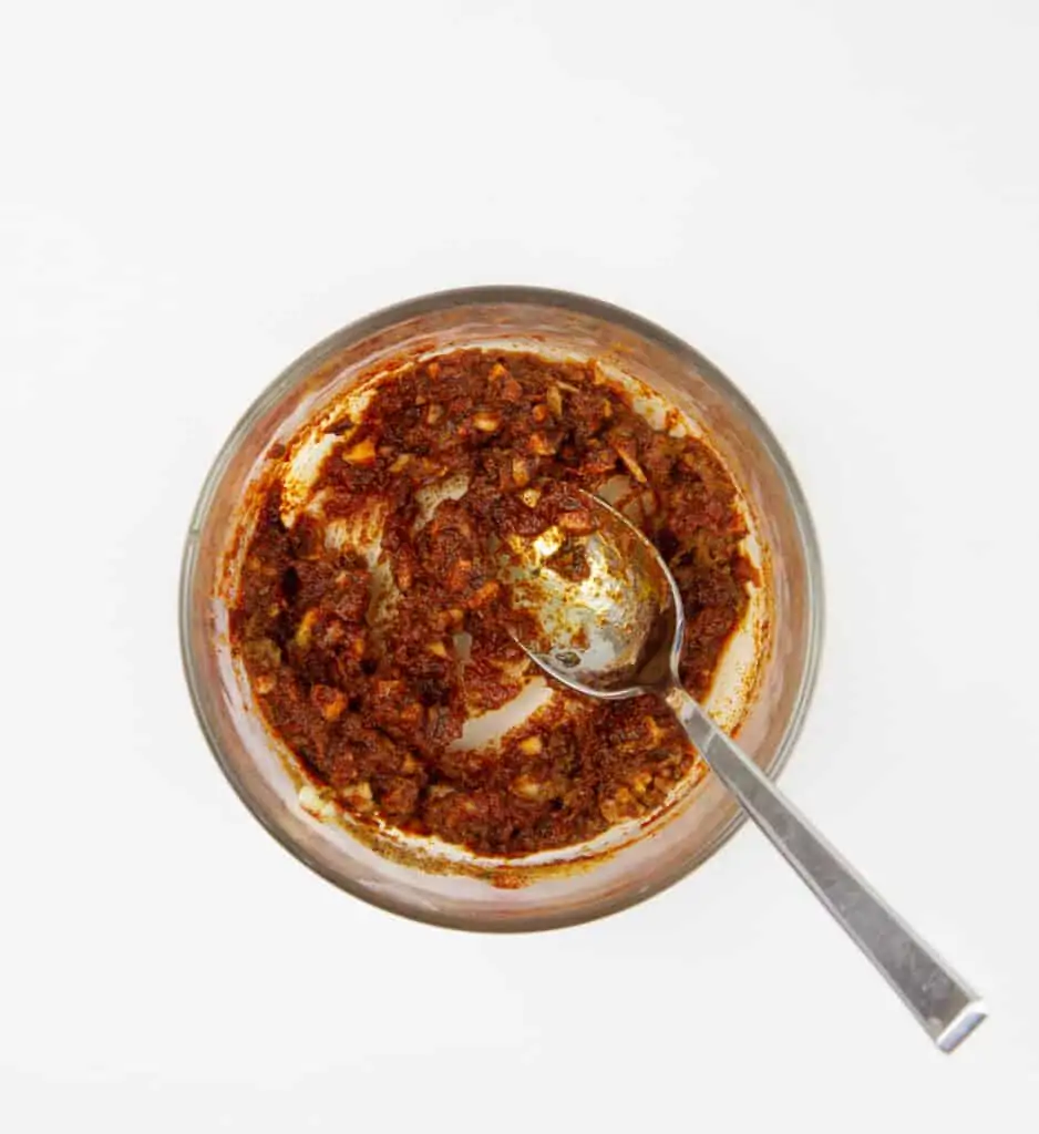 A small bowl and spoon containing the spice paste to marinade the chicken.