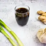 keto teriyaki sauce in a glass jar with garlic, ginger and scallions nearby