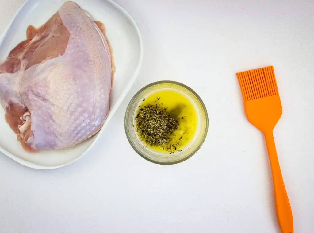 turkey breast with a bowl of herbed butter and a silicone brush to the side