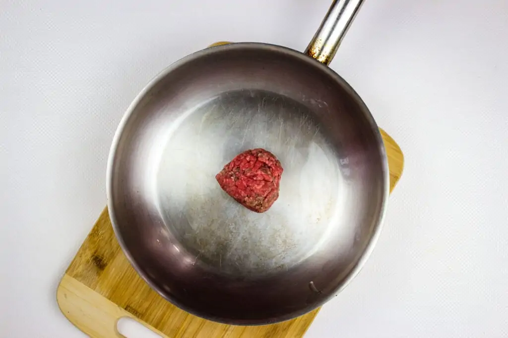 a heated skillet with a portion of ground beef in it