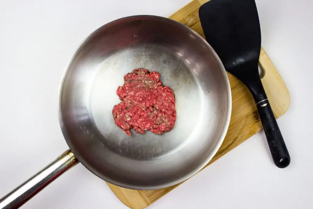 a hot skillet with a flattened beef patty in it with the flipper on the side