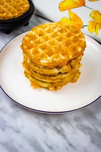 a stack of crispy chaffles on a plate with a second in the chaffle maker in the background
