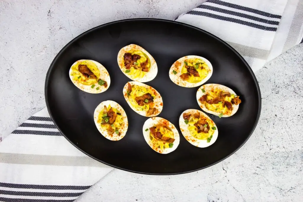 Finished keto deviled eggs with bacon on a black plate.