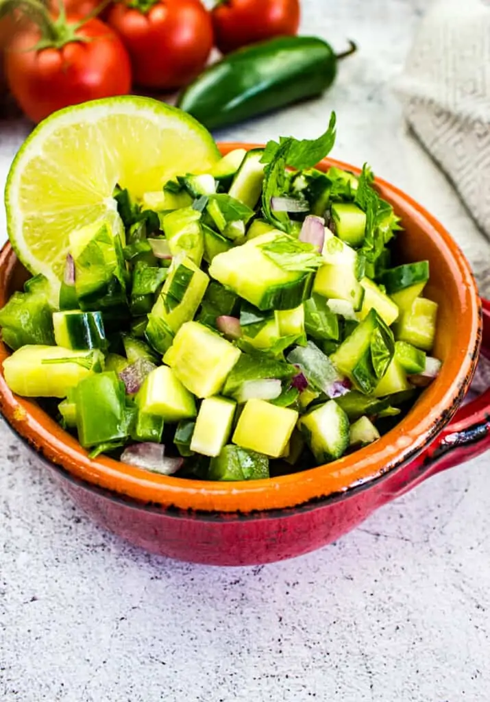 cucumber salsa in a bowl with tomatoes in the background