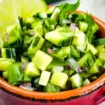 cucumber salsa in a bowl with tomatoes in the background