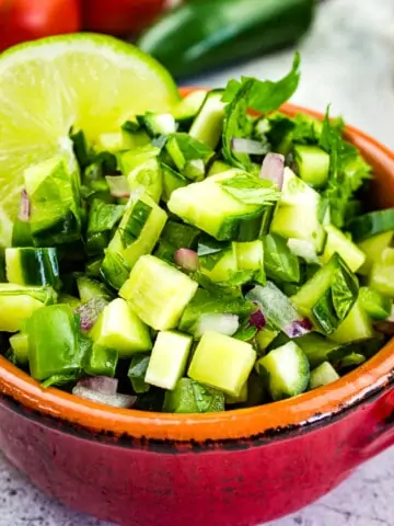 cucumber salsa in a bowl with tomatoes in the background