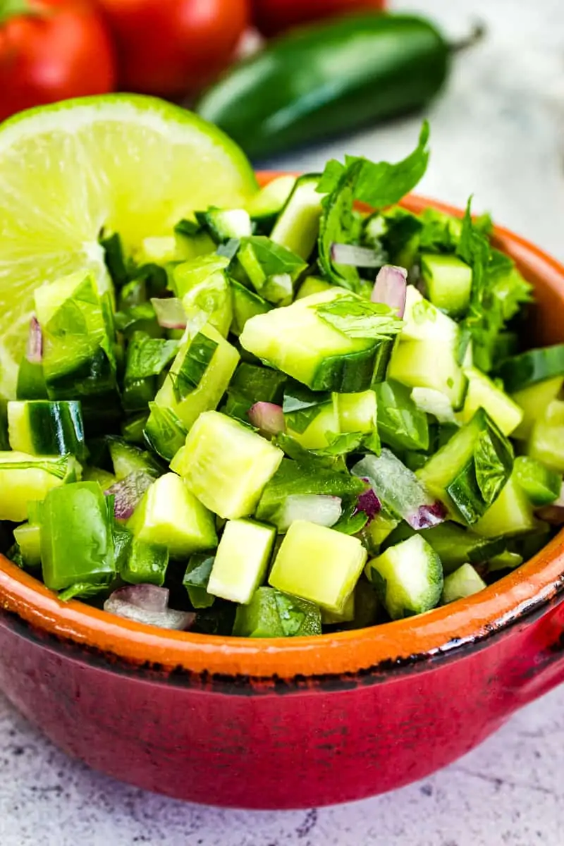 cucumber salsa in a bowl with tomatoes in the background