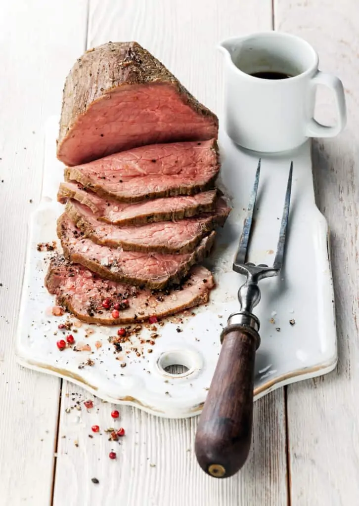 sliced roast beef on a board with a fork