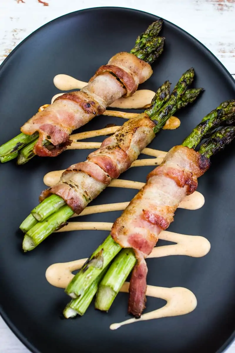 bacon-wrapped grilled asparagus on a black plate