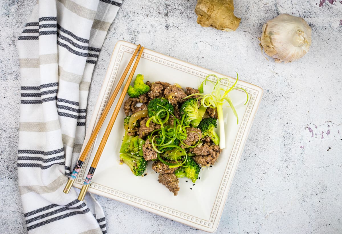 A square plate with Beef & Broccoli on it with chopsticks.