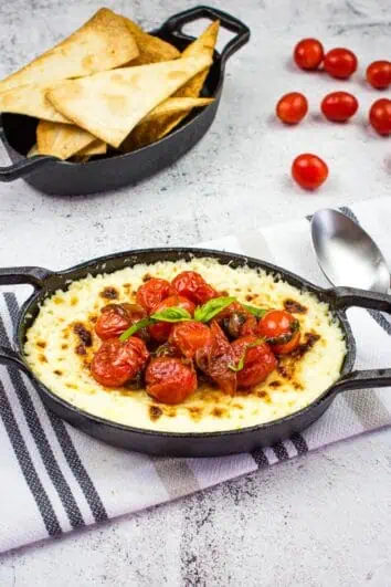 baked ricotta dip with parmesan and tomatoes in a black dish