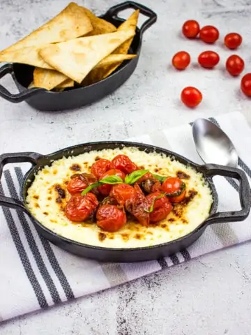 baked ricotta dip with parmesan and tomatoes in a black dish