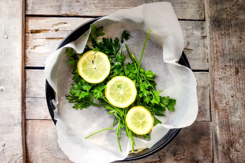 laying parsley and lemon in the bottom of a baking dish