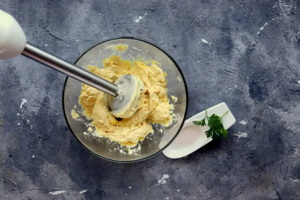 Mixing the yolk, cheese, chicken and herbs in a bowl to make keto spider deviled eggs.