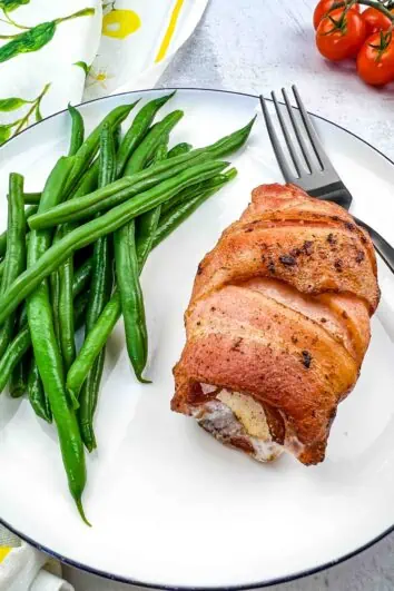 Keto bacon wrapped cod on a plate with green beans.