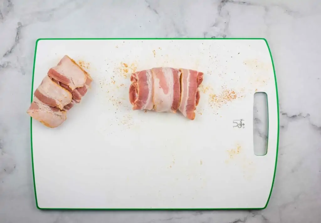 2 bacon wrapped filets of cod on a cutting board.