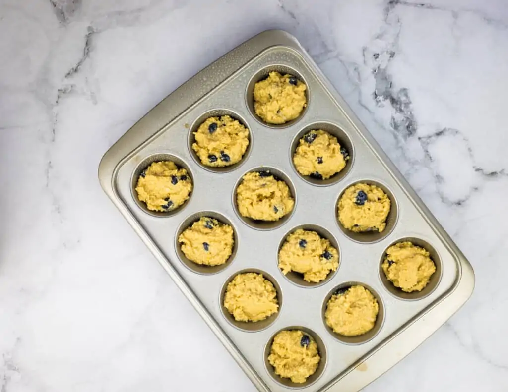 Filling muffin cups to make keto blueberry muffins