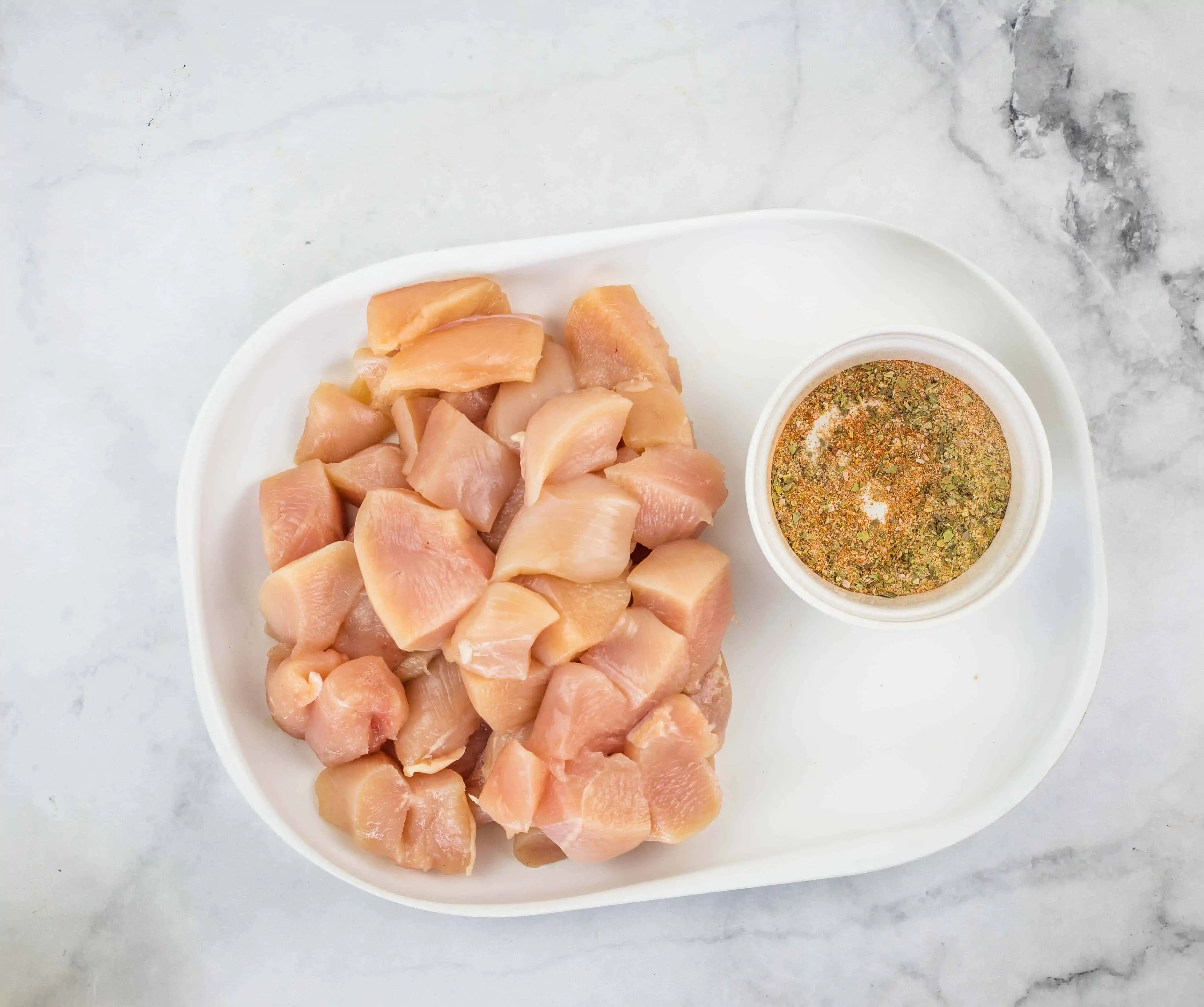 diced chicken on a plate with seasoning in a bowl