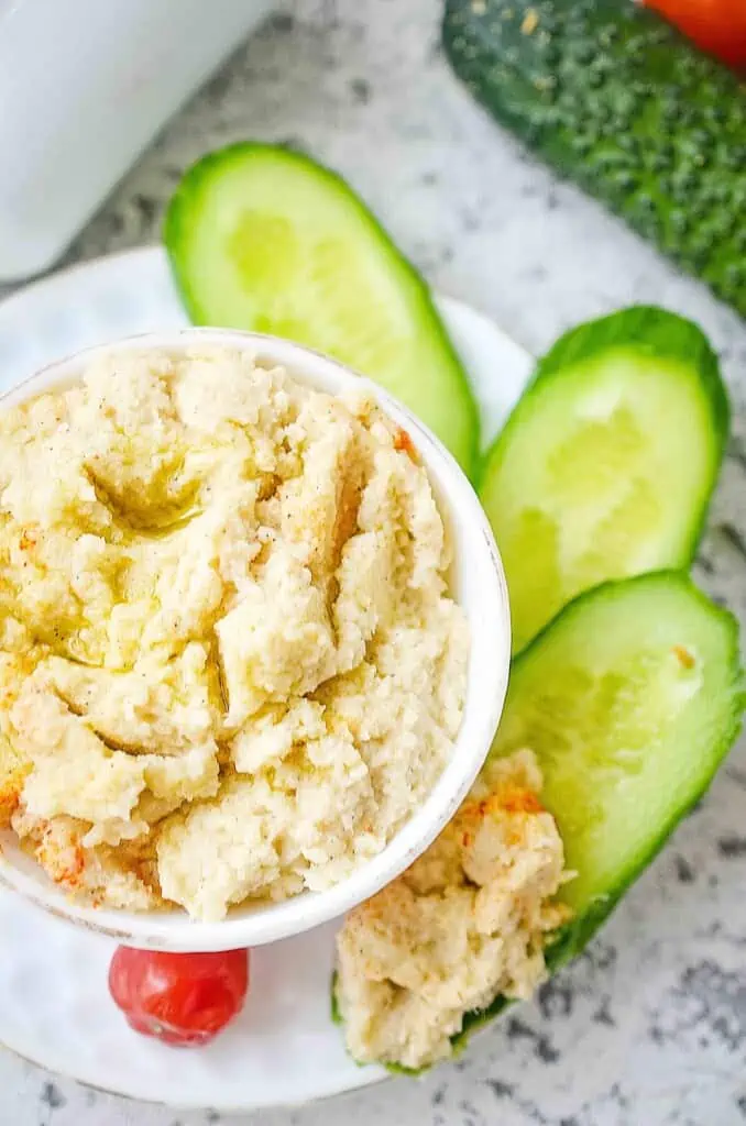 keto cauliflower hummus in a bowl with cucumbers on the side