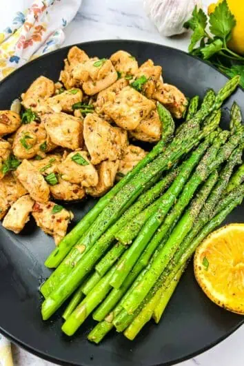 keto garlic butter chicken bites and lemon asparagus on a black plate