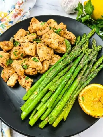 keto garlic butter chicken bites and lemon asparagus on a black plate