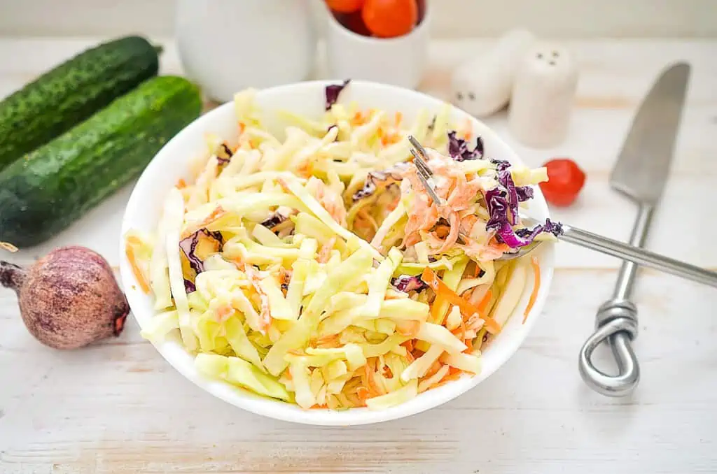 keto coleslaw in a bowl with vegetables in the background