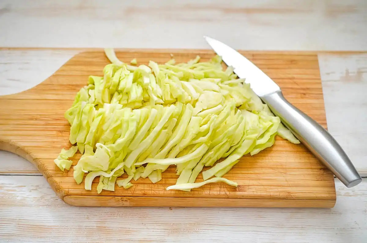 chopped cabbage and a knife on a cutting board to make keto coleslaw