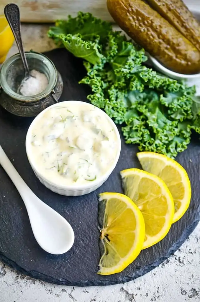 Keto tartar sauce on a black plate with lemon nearby.