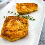 2 pieces of keto fried cod on a white plate with a sprig of thyme.