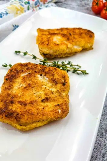 2 pieces of keto fried cod on a white plate with a sprig of thyme.