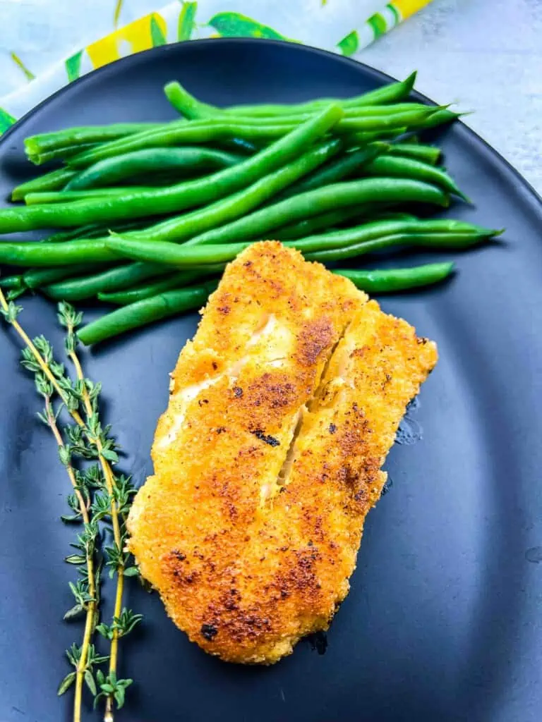 keto pan fried cod on a black plate with green beans.