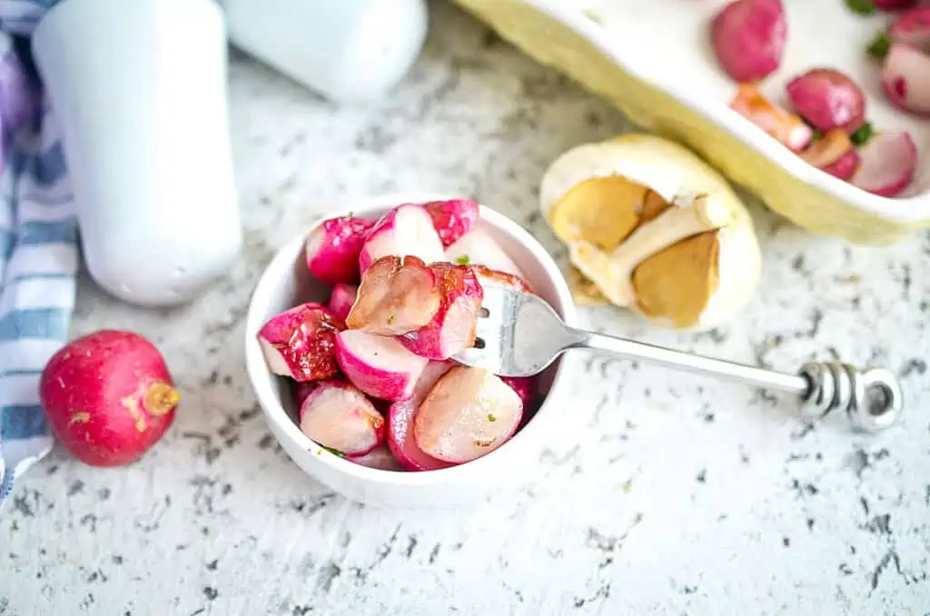 Roasted radishes in a small bowl with garlic nearby.