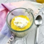 Keto lemon mug cake in a clear glass mug with a spoon to the side.