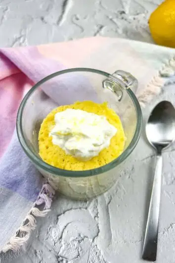 Keto lemon mug cake in a clear glass mug with a spoon to the side.