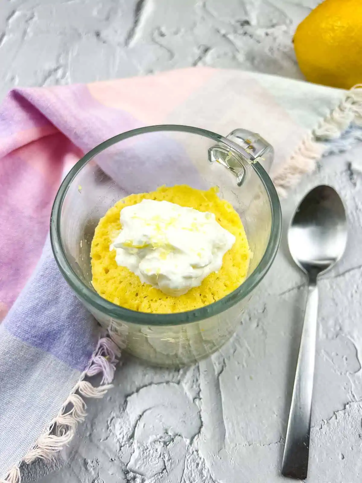 Keto lemon mug cake in a clear glass mug with a spoon to the side.