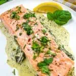 Baked Pesto Salmon on a round plate with wedge of lemon.