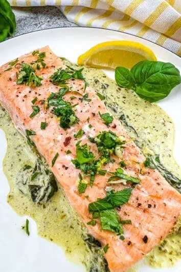 Baked Pesto Salmon on a round plate with wedge of lemon.