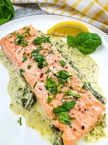 Baked Pesto Salmon on a round plate with wedge of lemon.